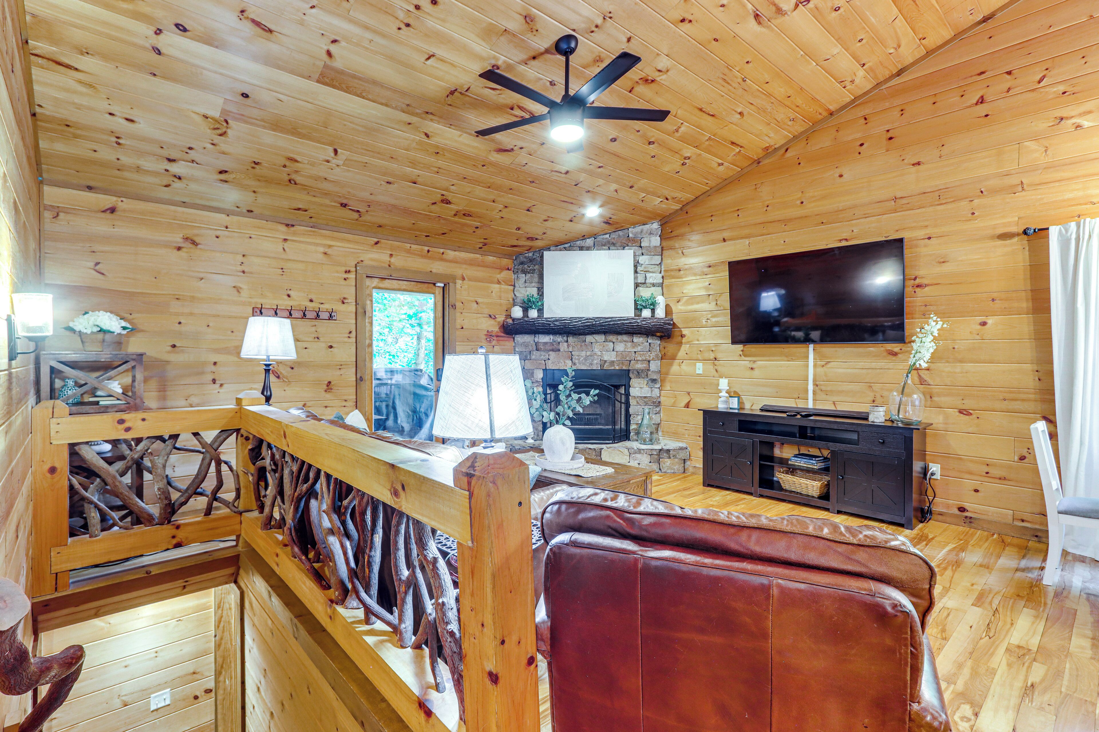 A wooden cabin interior with a fireplace, a television, and a wooden staircase.