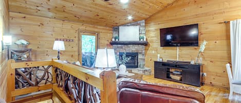 A wooden cabin interior with a fireplace, a television, and a wooden staircase.