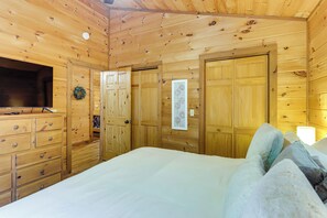 Ein Zimmer mit Holzboden, einem Bett, einem Schminktisch, einem Fernseher und einer Tür mit einer Dekoration.