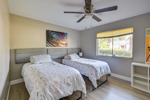 A bedroom with two beds, a ceiling fan, a window with blinds, and a painting on the wall.