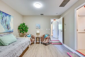 A modern hotel room with a bed, two chairs, a small table, a plant, and a painting on the wall.
