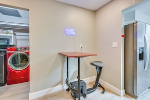 A compact kitchen with a washing machine, a refrigerator, and a small table with a chair.