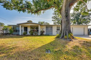 A single-story house with a front porch, a garage, and a large tree in the front yard.