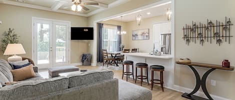 A modern living room with a grey sectional sofa, a dining area with a bar, and a kitchen with stainless steel appliances.