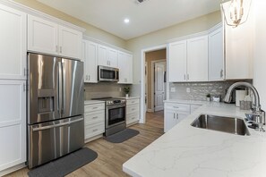A modern kitchen with stainless steel appliances, white cabinetry, and a marble countertop. - Golf, Grill & Relax! Brand-New Augusta Retreat (Augusta)