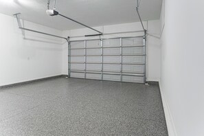 A garage with a metal door, a ceiling-mounted projector, and a speckled floor. - Golf, Grill & Relax! Brand-New Augusta Retreat (Augusta)