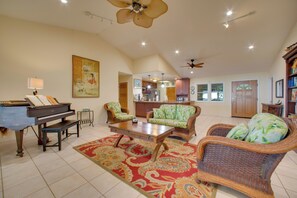 A spacious living room with a grand piano, comfortable seating, a large rug, and a ceiling fan.