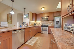 A kitchen with wooden cabinets, stainless steel appliances, granite countertops, and pendant lighting.