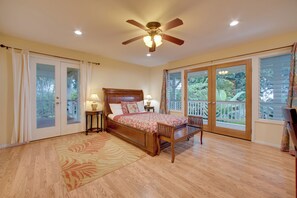 A bedroom with a wooden bed, two bedside tables with lamps, a ceiling fan, and large windows with a view of greenery. - Ocean-View Group Retreat! 8 Mi to Magic Sands (Holualoa)