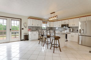 A kitchen with white cabinets, a stainless steel refrigerator, an island with bar stools, and a fire extinguisher on the wall. - Game Room & Countryside Views! Salvisa Family Gem (Salvisa)