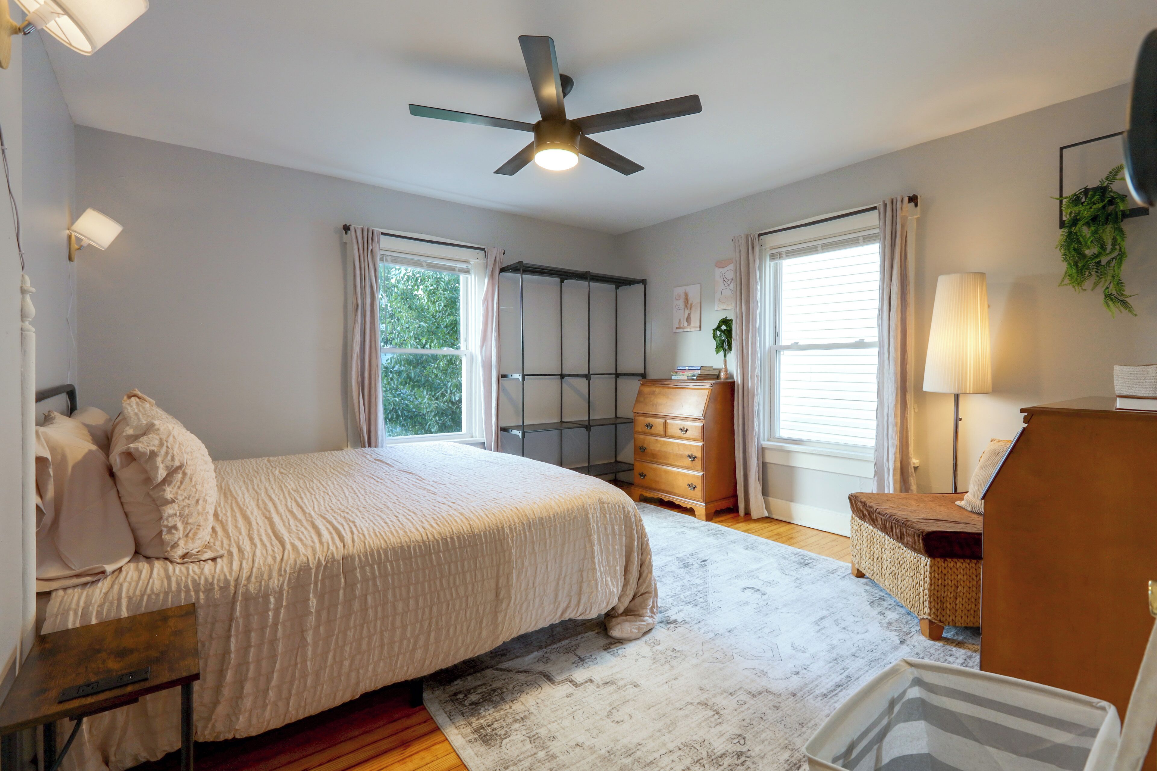 Une chambre à coucher comprenant un lit, une commode, un bureau, un ventilateur de plafond et une fenêtre.