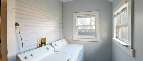 Un lavadero con lavadora blanca, secadora y ventana.