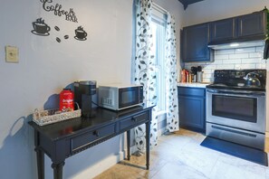 A kitchen with a coffee maker, microwave, and kettle on the counter, a coffee machine, and a kettle on the stove.