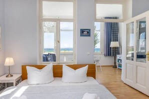A hotel room with a bed, a nightstand, a lamp, and a view of the sea through large windows. - Beach bliss at Villa Agnes (Binz)
