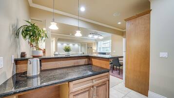 A kitchen with granite countertops, wooden cabinets, a coffee maker, and pendant lighting.