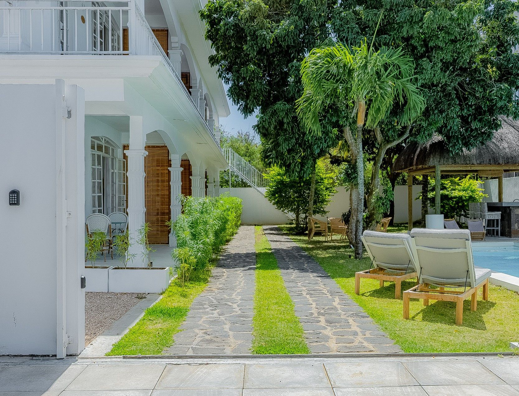 Un hôtel doté d’un chemin pavé menant à un espace piscine, entouré de verdure et agrémenté de sièges extérieurs.