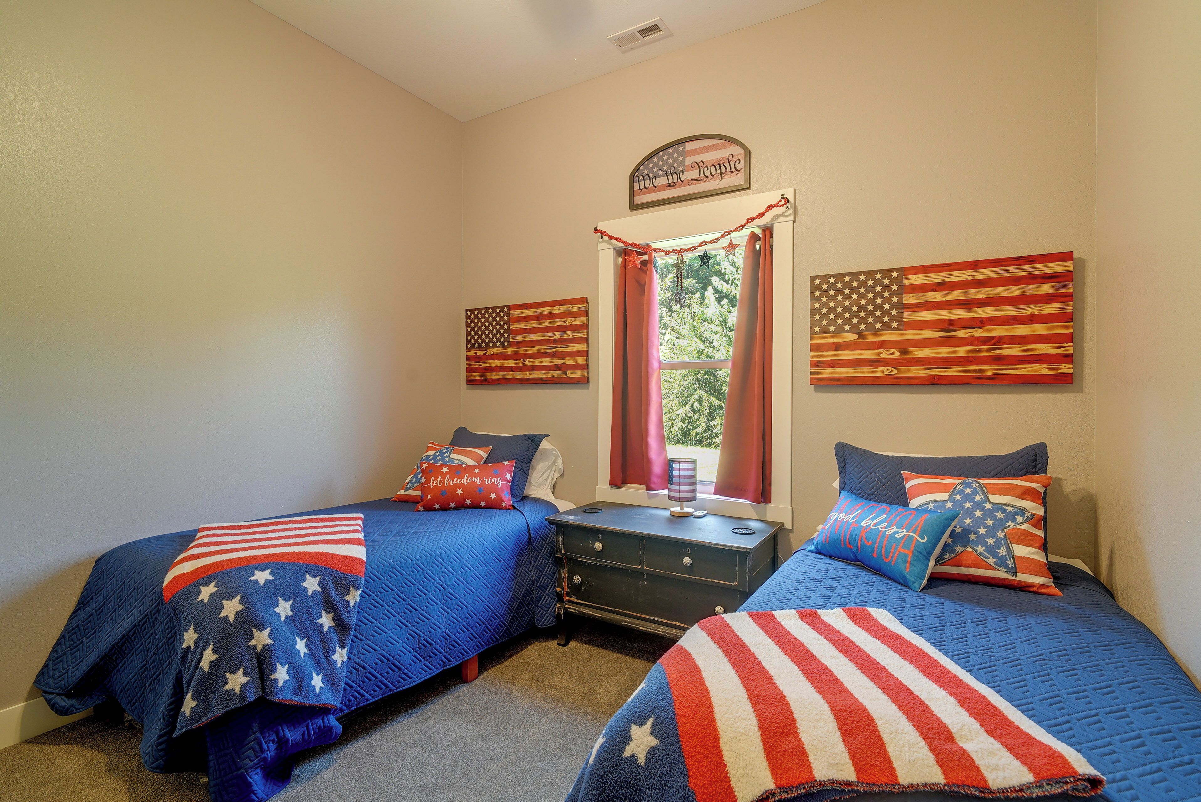 A bedroom with two beds, each covered with a blue quilt featuring white stars, and a window with red curtains.