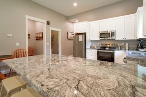 A kitchen with white cabinets, a stainless steel refrigerator, a microwave, and a granite countertop.