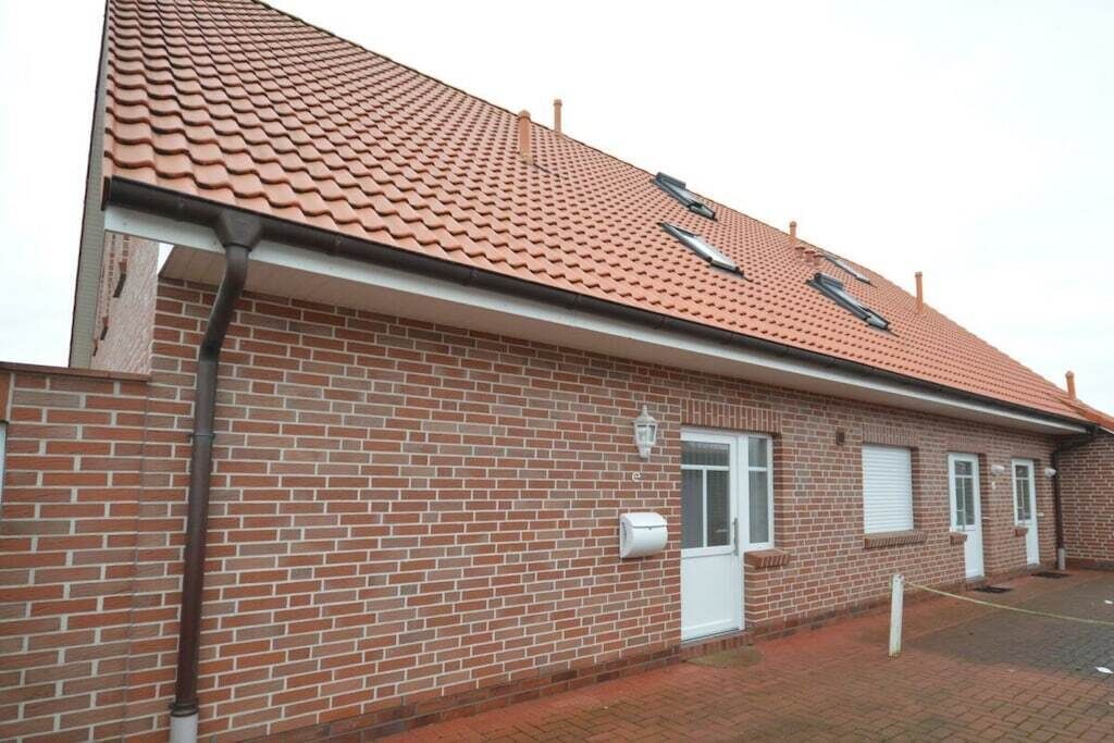 Un bâtiment de deux étages en briques, avec un toit recouvert de tuiles rouges, une porte blanche et une petite fenêtre.
