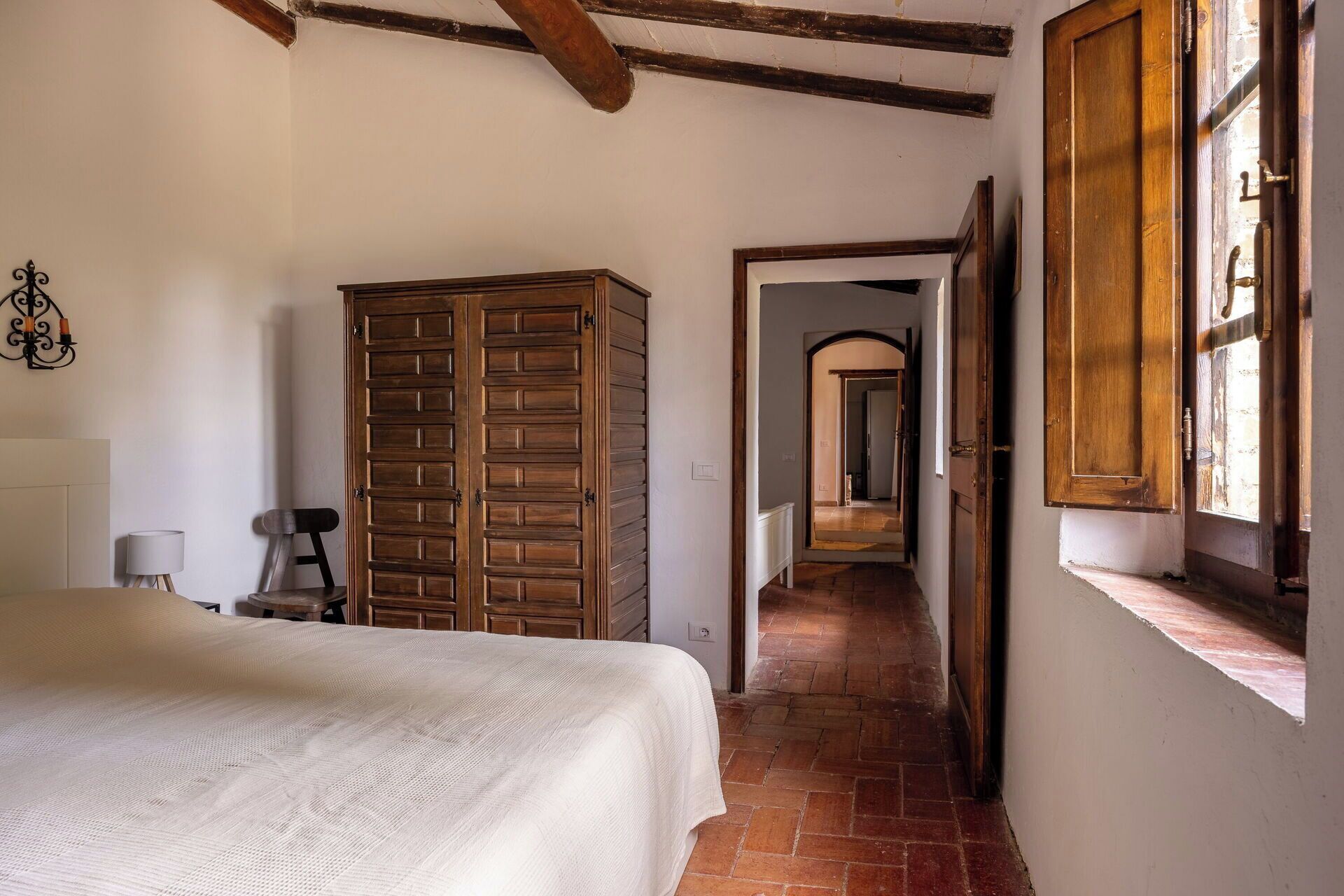 A bedroom with a bed, a wooden wardrobe, a lamp, and a window with a view.