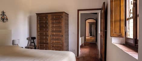 A bedroom with a bed, a wooden wardrobe, a lamp, and a window with a view.