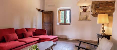 Una habitación con sofá rojo, una mesa de centro de madera, una silla, una lámpara y un ventanal con vistas al verdor.