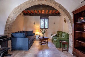 A cozy living room with a stone archway, a blue sofa, a green sofa, a wooden coffee table, and a bookshelf. - Casa Clara Pool, Casole Elsa, Monti (Casole D'elsa)