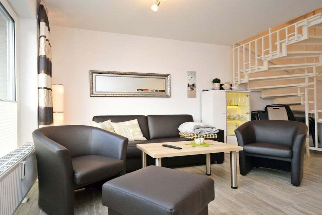 Een moderne woonkamer met een bank, twee fauteuils, een salontafel en een trap.