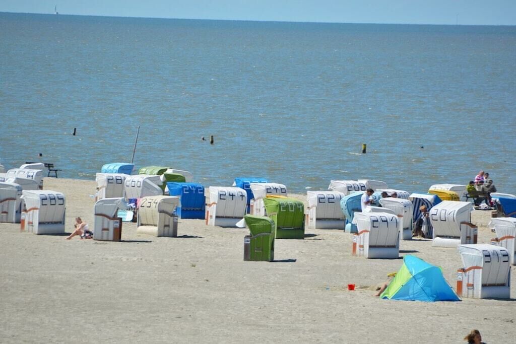 A beach with rows of numbered beach huts and a tent.