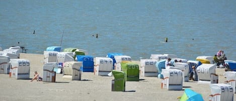 A beach with rows of numbered beach huts and a tent.