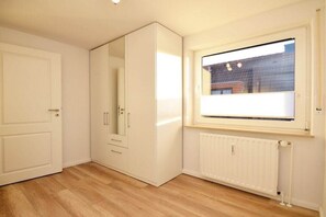 Une pièce avec une armoire blanche, un radiateur et une fenêtre donnant sur des immeubles.