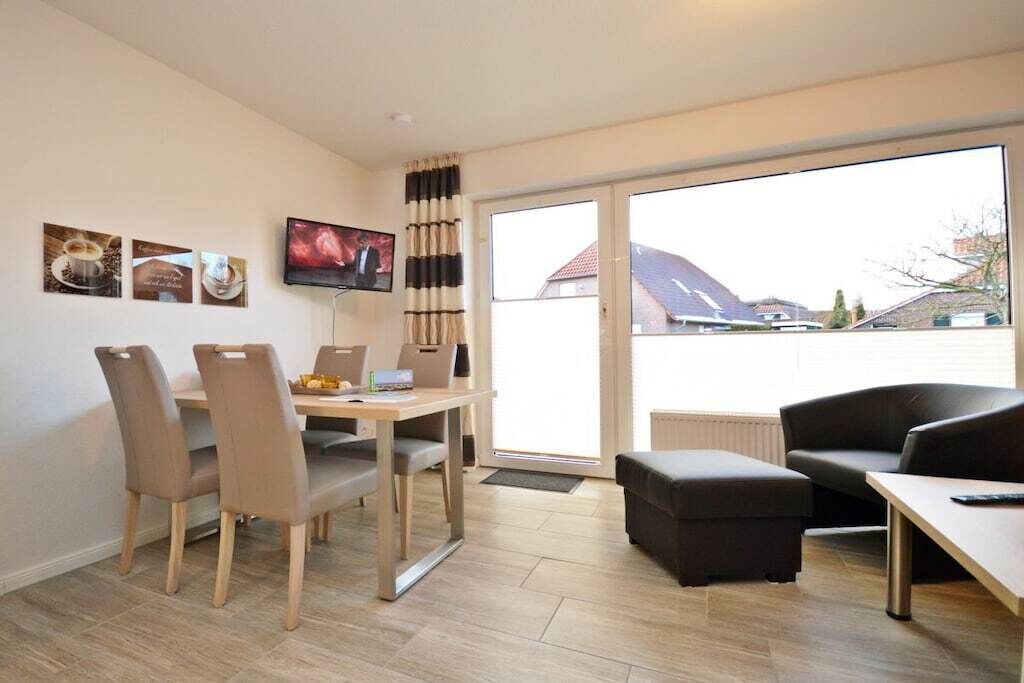 A modern living room with a dining area, a flat-screen TV, and a large sliding glass door leading to a balcony.