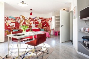 A modern living room with a vibrant abstract mural, a dining area with a white table and red chairs, and a television mounted on the wall. - A Midsummer Night's Dream at Karoline's House (Binz)