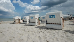 Cadeiras de praia numeradas 828, 686, 824 e 847 numa praia de areia sob um céu nublado.