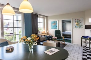 A room with a dining table, a sofa, a chair, and a bunk bed. There are windows, artwork on the walls, and a checkered floor. - The good life in Karoline's house (Binz)