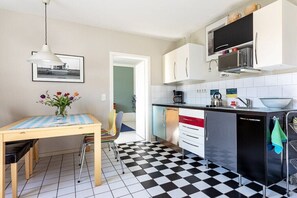 Eine kleine Küche mit Schachbrettboden, einem Esstisch mit Stühlen und einem Kühlschrank.