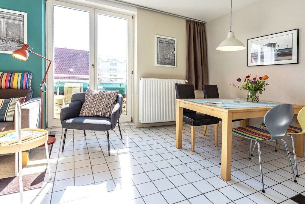 A room with a dining table, chairs, a sofa, a radiator, and a window with curtains.