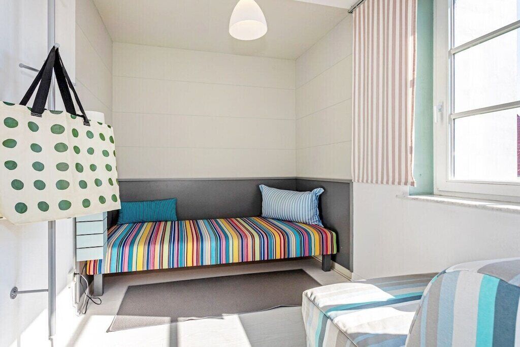 Ein kleiner, gemütlicher Raum mit einem gestreiften Bett, einem Fenster mit gestreiften Vorhängen und einer gepunkteten Tasche an der Wand.