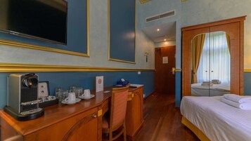 Quarto de hotel com cama, escrivaninha com cafeteira, televisão e espelho.
