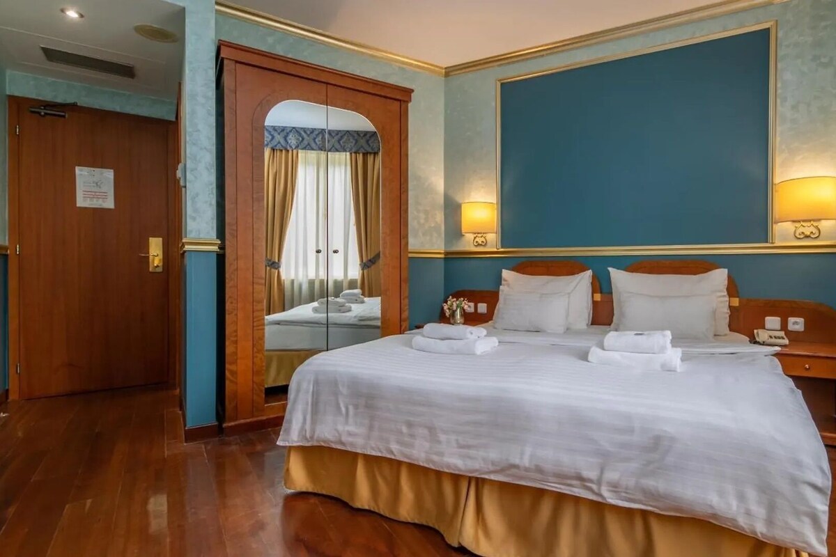 A hotel room with a large bed, two bedside tables, a mirror, and a wooden door.