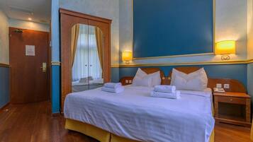Una habitación de hotel con una cama grande, dos mesitas de noche, un armario de madera y una ventana con cortinas.