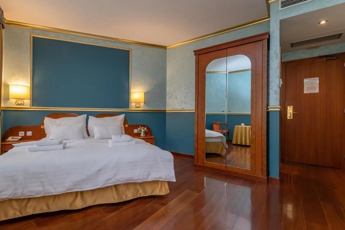 A hotel room with a large bed, bedside lamps, a mirror, and a wooden door.