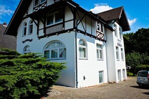 A two-story building with a balcony, large windows, and a gravel driveway. - Holiday apartment with 2 bedrooms (Travemünde)