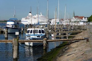 Ein Yachthafen mit vor Anker liegenden Booten, ein Kreuzfahrtschiff im Hintergrund und eine Holzstele.