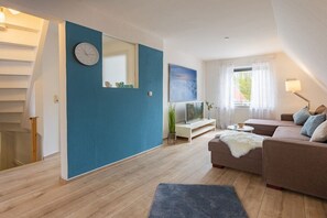 A modern living room with a blue accent wall, a sofa set, a television, and a staircase. - Holiday apartment with 2 bedrooms (Travemünde)