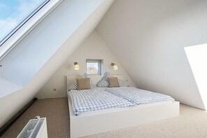 Ein Schlafzimmer mit schrägem Dach, einem Bett mit karierter Bettwäsche, zwei Wandleuchten und einem Fenster.