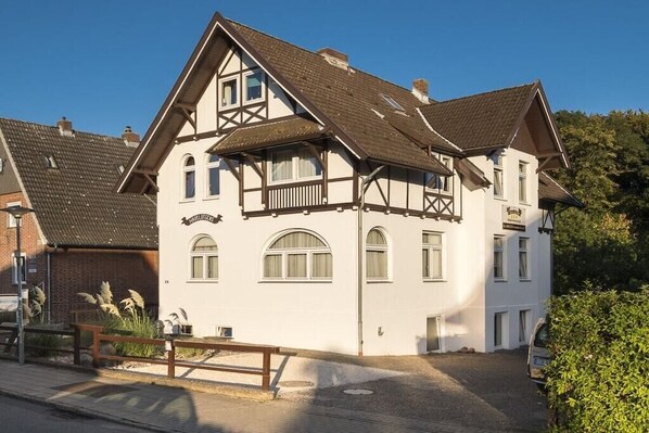 A traditional half-timbered building with a balcony, a small garden, and a paved driveway. - Holiday apartment with 1 bedroom (Travemünde)