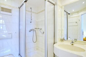 A bathroom with a glass-enclosed shower, a white sink, and a mirror. - Holiday apartment with 1 bedroom (Travemünde)