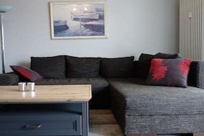 A modern living room with a sectional sofa, a small table, and a painting on the wall. - in the house Stranddüne, No. 14 (Haffkrug)