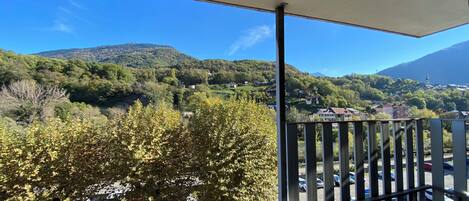 A balcony with a view of a mountainous landscape, trees, and a parking area.